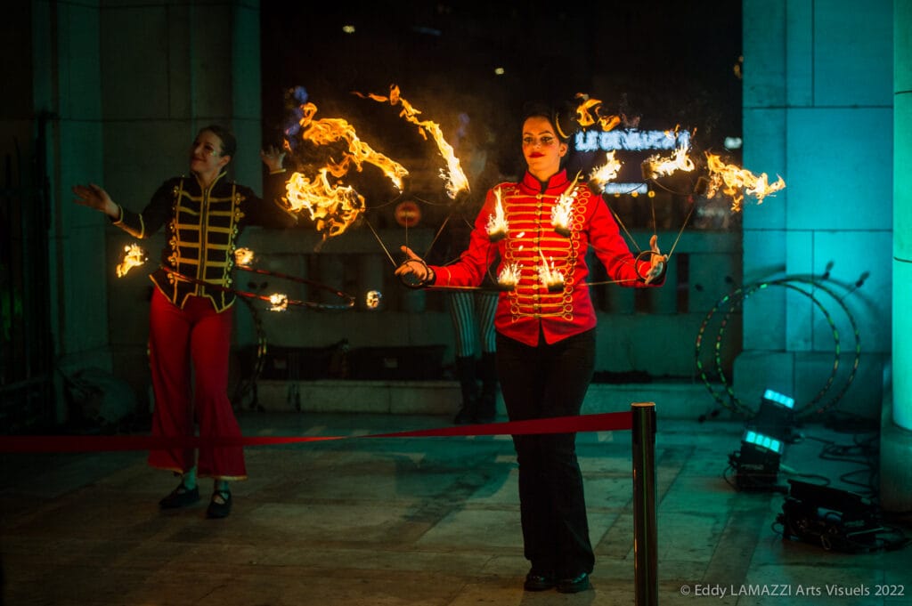 Un artiste en veste rouge avec des objets enflammés, de nuit, spectacle Cirk’n’Swing