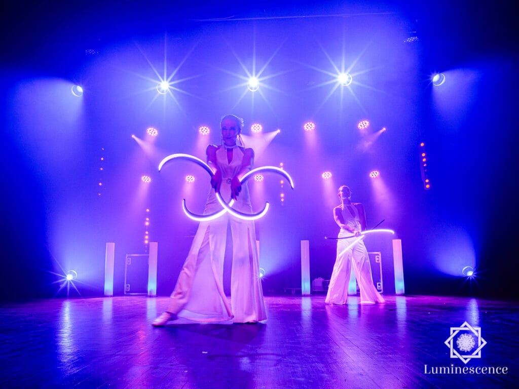 Deux artistes avec des cerceaux LED lumineux sur une scène éclairée en bleu