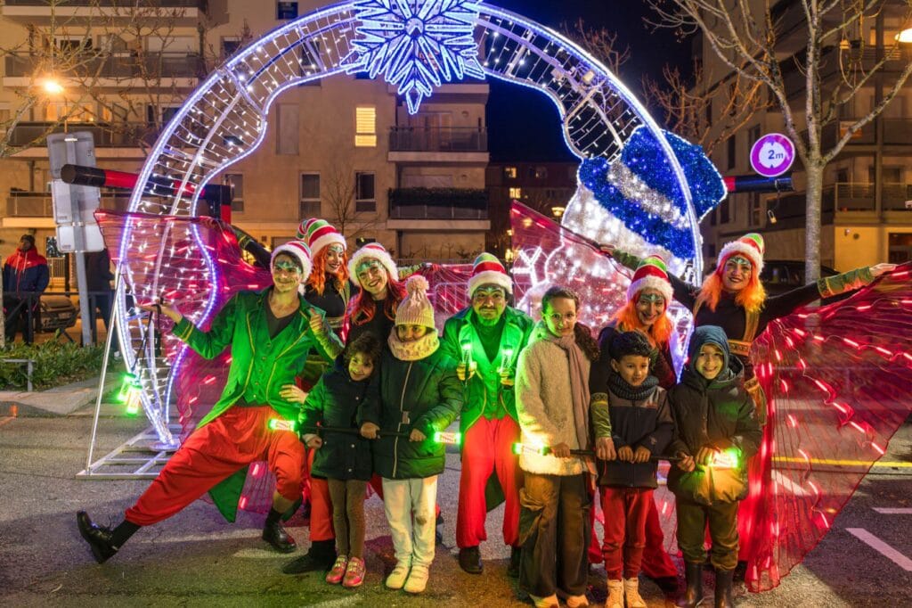 Des artistes en costumes de lutins devant des arches lumineuses de Noël